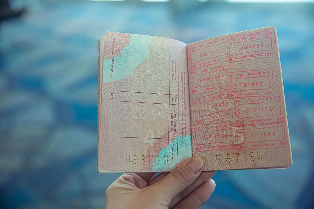An open passport with colorful travel stamps, held in hand inside an airport terminal.